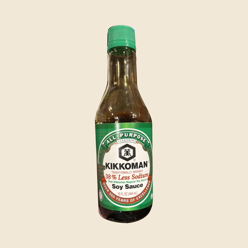 Complete green-capped Kikkoman Less Sodium Soy Sauce 15 fl oz bottle on a beige background