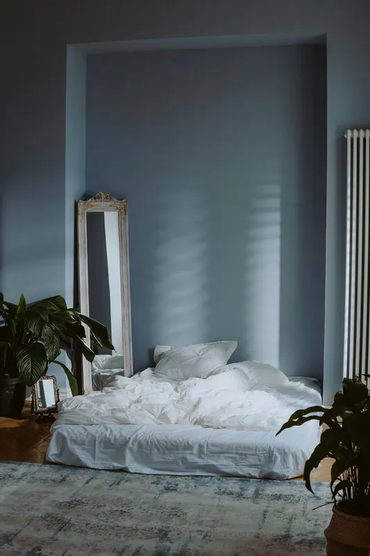 Serene minimal bedroom interior with soft natural lighting and green potted plants creating a peaceful atmosphere