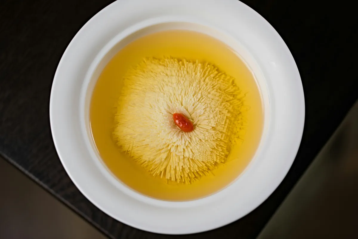 Dried yellow chrysanthemum flowers steeping in a white ceramic bowl of tea