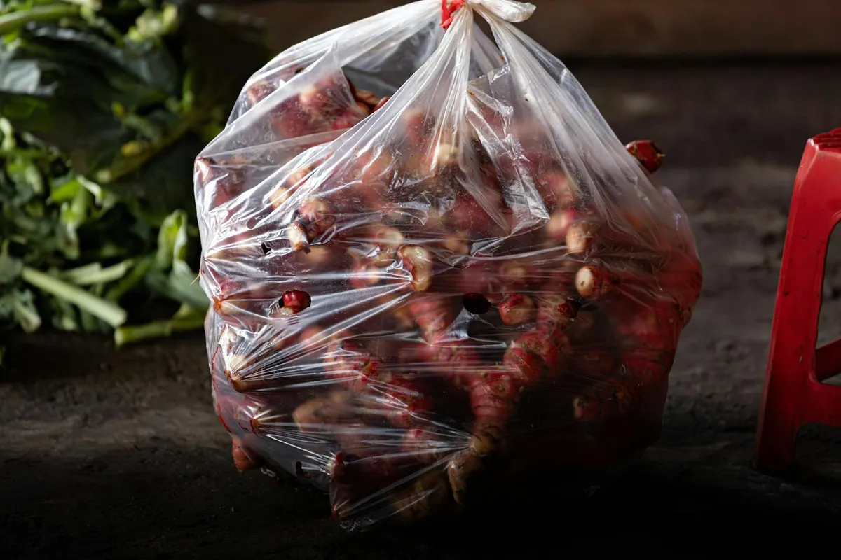 Bag of fresh galangal rhizomes with reddish-pink skin displayed at a Vietnamese market stall